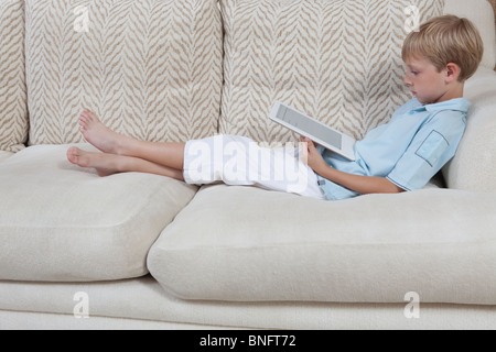 Boys sits on sofa reading a digital book Stock Photo