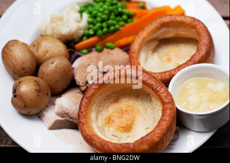 Roast pork served with boiled potatoes, cauliflower, carrots, peas, Yorkshire puddings, apple sauce, and gravy on Sunday. Stock Photo