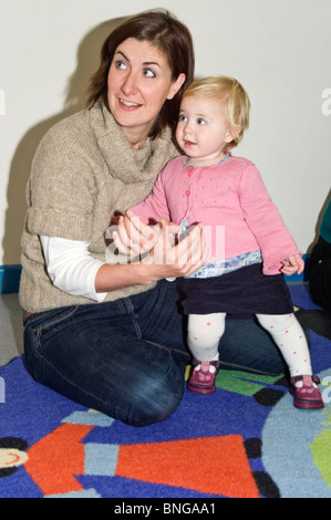 Vertical portrait of a young mum with her baby daughter at a 'Parent and Toddler' class. Stock Photo