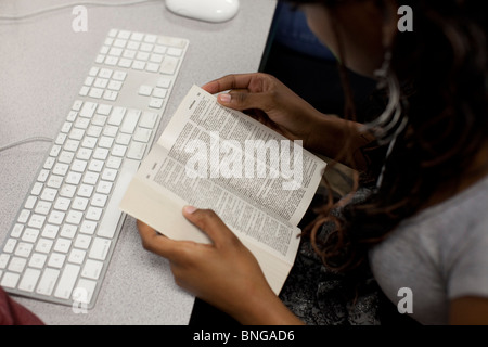 Female African-American student looks up word in dictionary while working on computer at Manor New Tech High School Stock Photo