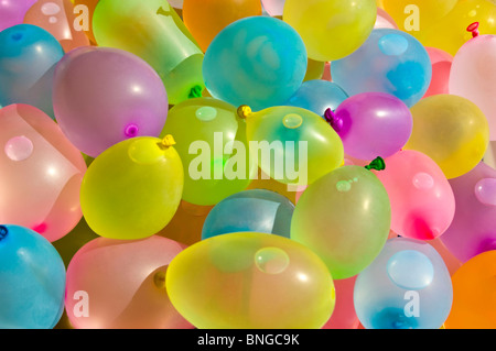 Horizontal close up of hundreds of colourful latex balloons filled with water in preparation for a water fight. Stock Photo