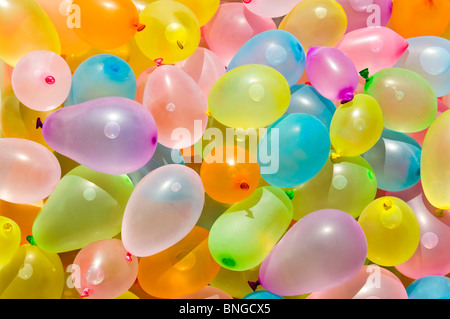 Horizontal close up of hundreds of colourful latex balloons filled with water in preparation for a water fight. Stock Photo