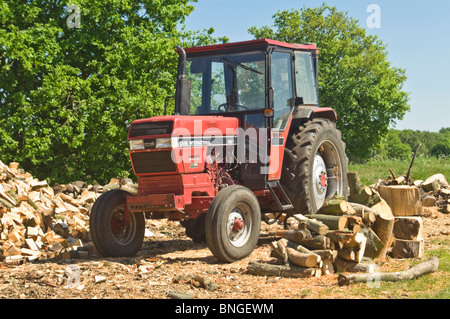 Horizontal close up of a bright red Case International tractor parked up by a large wood pile in the sunshine. Stock Photo