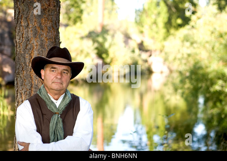 Handsome older cowboy, leaning against a tree Stock Photo