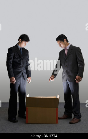 Two businessmen looking into an illuminated cardboard box Stock Photo
