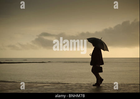 A man sheltering under an umbrella on a wet summer evening, Aberystwyth Wales UK Stock Photo