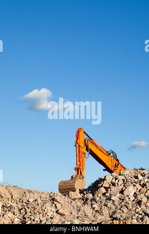 An excavator sits on a pile of rubble with blue sky after demolishing a building Stock Photo