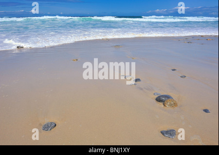 Romantic beach turquoise blue waves ebb flow on sandy shore with stones rocks horizon over water and reflections in sand Stock Photo