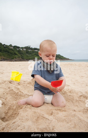 Baby boy 14 months old playing on the beach with a bucket and spade Carbis Bay beach, St Ives, Cornwall, England, United Kingdom. Stock Photo