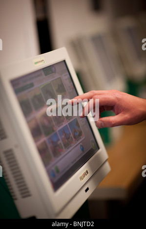 Customer using a touch screen computer terminal to chose and order prints at a high street photo processing lab, UK Stock Photo