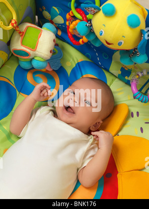 Happy smiling six week old cute baby boy lying in a colorful play mat with toys Stock Photo