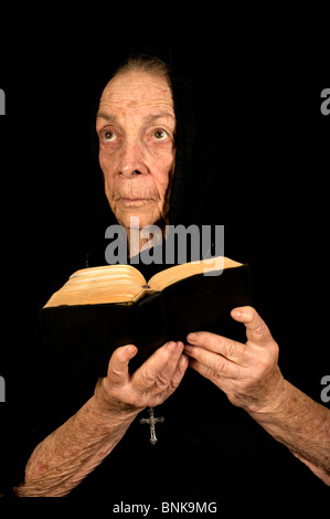 Old Women Deep in Prayer holding a Bible and Rosary Stock Photo