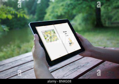 A woman reading Winnie the Pooh story on an iPad at outdoor park Stock Photo
