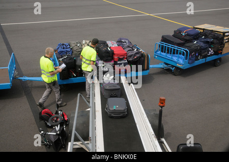 Airport baggage handler loading bags from a trolley onto an aircraft at Beziers International Airport southern France EU