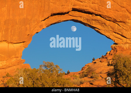 Arch Windows Section Red Rocks sunlight moon persons sitting blue sky rock formations Nature Landscape Arches National Park Stock Photo