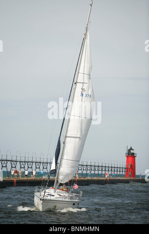 sail boat sails along the pier and lighthouse from Lake Michigan into the Black river in South Haven Michigan Stock Photo