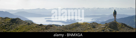 A hiker stands on top of the Juneau Ridge looking toward Auke Bay with the Chilkat Mt. Range in the background, Juneau, Alaska Stock Photo