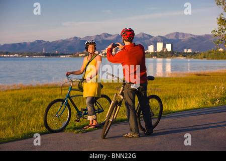 Bicyclists rest and take self-portraits along the Tony Knowles Coastal Trail with Anchorage in the background, Alaska Stock Photo