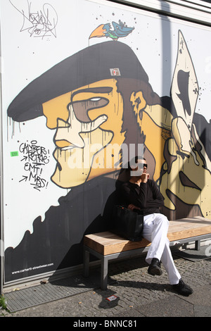 A young man sitting on a bench in front of a poster, Berlin, Germany Stock Photo