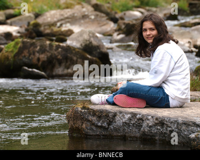 Young girl sat on a rock beside the East Lyn river,  Lynmouth, Devon, UK Stock Photo