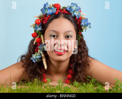 Summer woman with strawberries, fruit and flowers in her hair lying in green grass Stock Photo