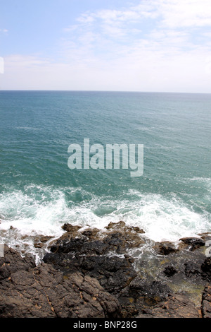 Waves crashing on rocks below small cliff Stock Photo