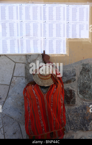 A Quechua man wearing traditional dress looks for his name on the electoral roll on wall outside the Town Hall, Ollantaytambo, Sacred Valley, Peru Stock Photo