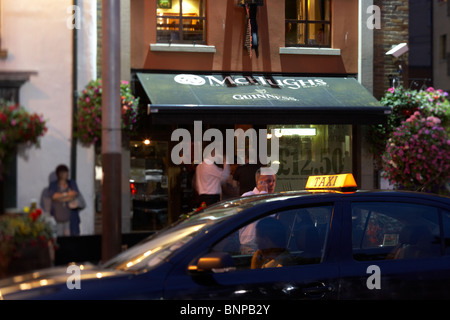 man on a mobile phone gets in to a taxi outside McHughs pub at night in Belfast city centre Northern Ireland UK. Stock Photo