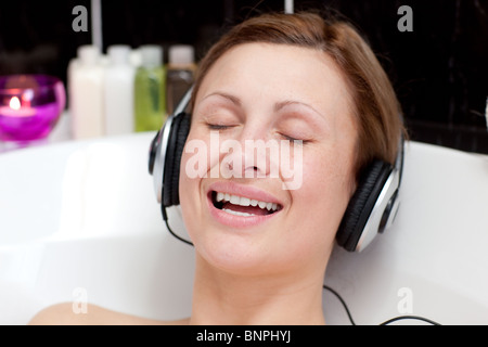 Smiling young woman listening music  in a bubble bath Stock Photo