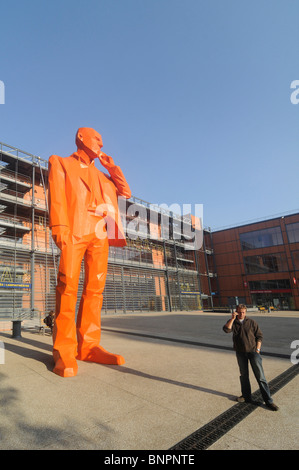 A man using his mobile phone near a giant statue showing a man with a mobile phone in the cité internationale in Lyon, France. Stock Photo