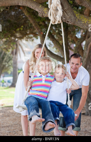 Happy parents pushing their children on a swing Stock Photo