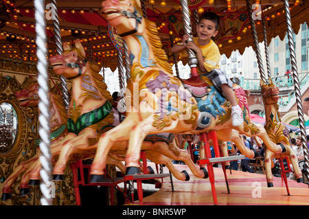 Young boy enjoys an old fashioned carousel style fair ground ride on Brighton beach. Brighton, East Sussex. Stock Photo