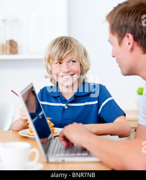 Cute boy having breakfast while his father using a laptop Stock Photo