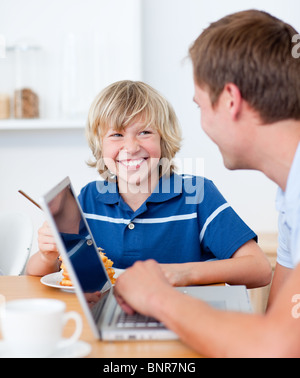 Smiling boy having breakfast while his father using a laptop Stock Photo