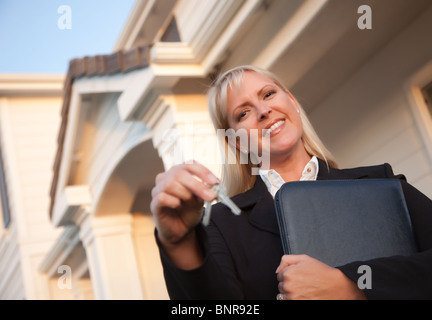 Female Real Estate Agent Handing Over Keys in Front of Beautiful House. Stock Photo