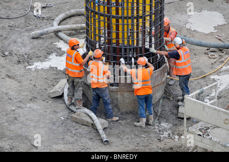 Building construction site workers in team work working together place steel cage held by crane in pile casing foundations Canary Wharf Crossrail UK Stock Photo