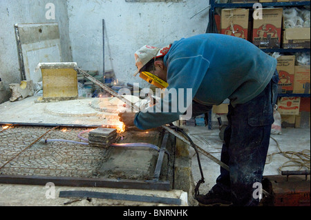 A man welding the metal supports in the construction of a ceramic fountain at a pottery in Fes, Morocco Stock Photo