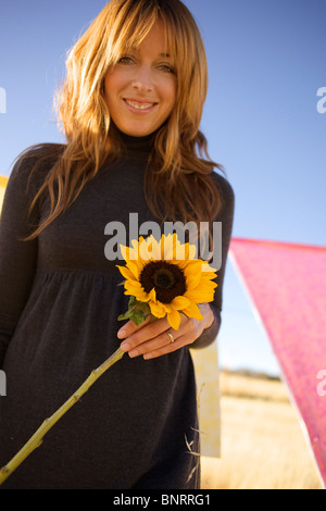 Female holds a sun flower and smiles. Stock Photo