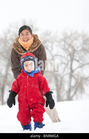 A two year old boy plays in a snowy field during a snowstorm in a red snowsuit with his mother in a park, Fort Collins, Colorado
