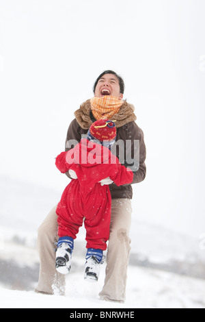 A two year old boy plays in a snowy field during a snowstorm in a red snowsuit with his mother in a park, Fort Collins, Colorado Stock Photo