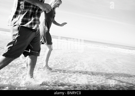 Couple run by the water and get their feet wet at the beach. Stock Photo