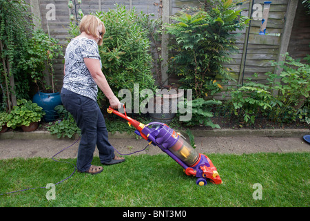 Woman Vacuuming the grass lawn with a Dyson vacuum cleaner Stock Photo