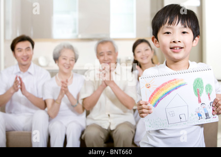 Little boy holds up a drawing in front of his family Stock Photo
