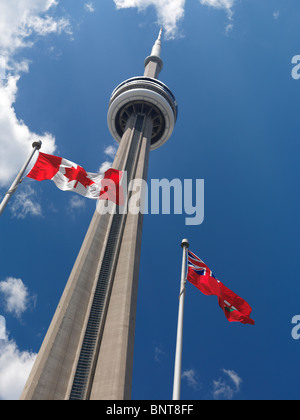 Ontario and Canada flags flying in front of Toronto CN tower over blue sky Stock Photo