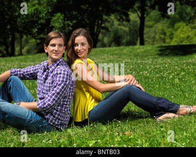 Young happy smiling couple in their early thirties sitting on grass in a park Stock Photo