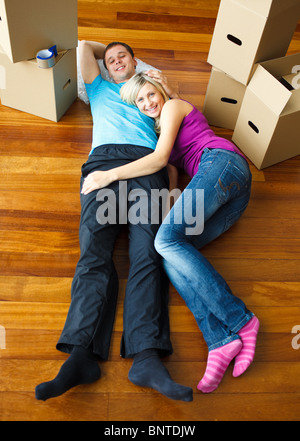 Happy couple relaxing on the floor with boxes around Stock Photo