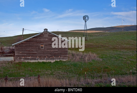 This rural farmland depicts an old rustic barn on gently rolling hills with an old fashioned wind mill in the pasture land Eastern Washington state. Stock Photo