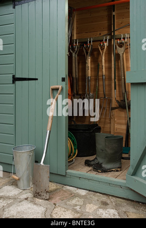 Spade and muddy boots by a garden shed. Stock Photo