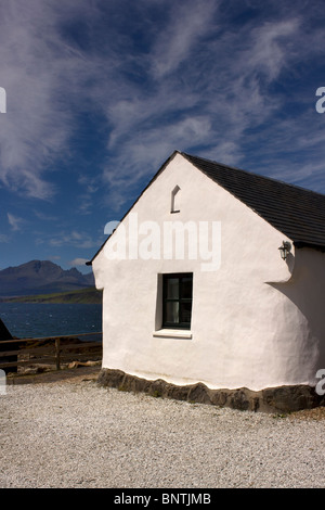 Sunlit white cottage at Ord on the Isle of Skye with a brilliant blue sky, Loch Eishort and Cuillin Mountains behind. Stock Photo
