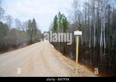 Man walks unpaved road leading into water during spring floods Stock Photo
